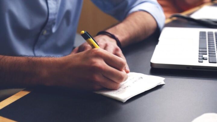 Personne prenant des notes à côté d'un ordinateur