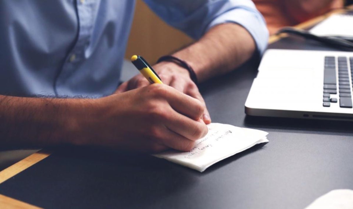 Personne prenant des notes à côté d'un ordinateur